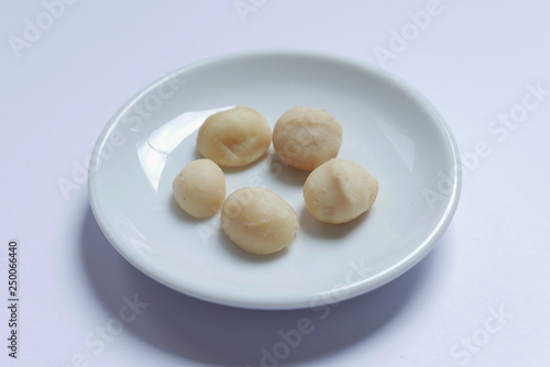 Top view of macadamia nuts in bowl on white background.