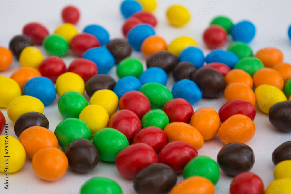 A scattering of colored small chocolates on a white background. Soft focus A scattering of colored small chocolates on a white background. Soft focus
