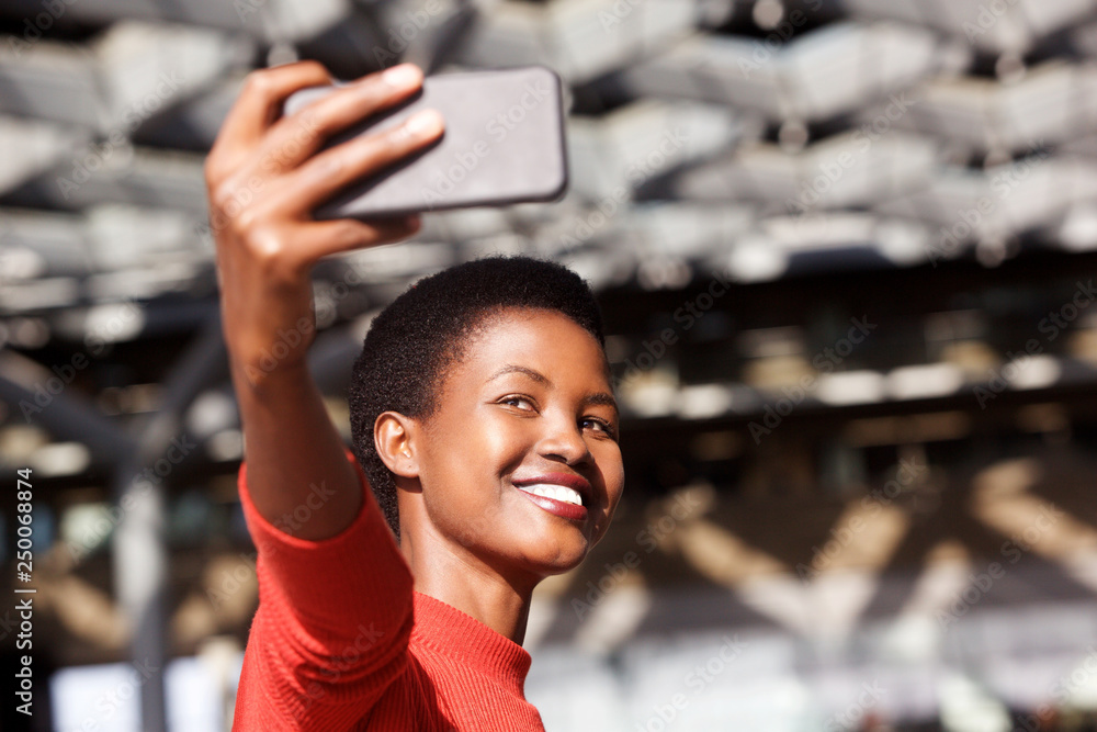 Fototapeta premium smiling young african woman taking selfie with cellphone camera