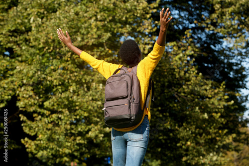 behind of young black woman with arms outstretched in park