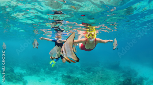 Happy family - mother, kid in snorkeling mask dive underwater, explore tropical fishes Platax ( Batfish). Travel lifestyle, beach adventure, swimming activity on summer with child. Focus on fishes