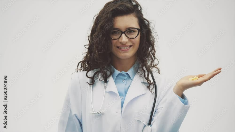 Attentive young doctor girl in a medical dressing gown holding a drug jug in his hand. Woman is isolated on a gray background. Conception of treatment, hospital. Attentive young doctor girl in a medical dressing gown holding a drug jug in his hand. Woman is isolated on a gray background. Conception of treatment, hospital.