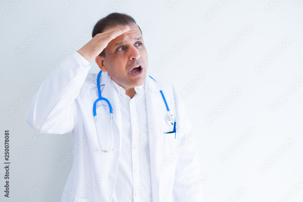 Middle age doctor man wearing stethoscope and medical coat over white background very happy and smiling looking far away with hand over head. Searching concept. Middle age doctor man wearing stethoscope and medical coat over white background very happy and smiling looking far away with hand over head. Searching concept.