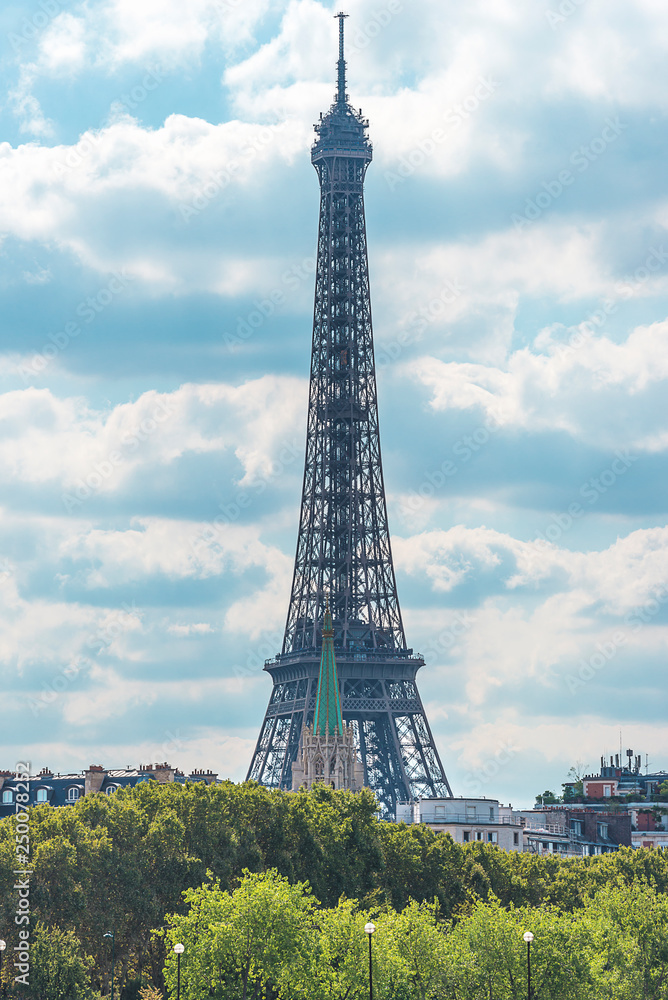 Beautiful view of Eiffel Tower against the white clouds on the blue sky on sunny summer day. Vertical picture