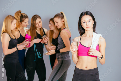 Group of six smiling sportive girls standing together talking and laughing after training, diverse happy toned women relax after workout, have break drinking water, chatting and having fun in studio © Iryna