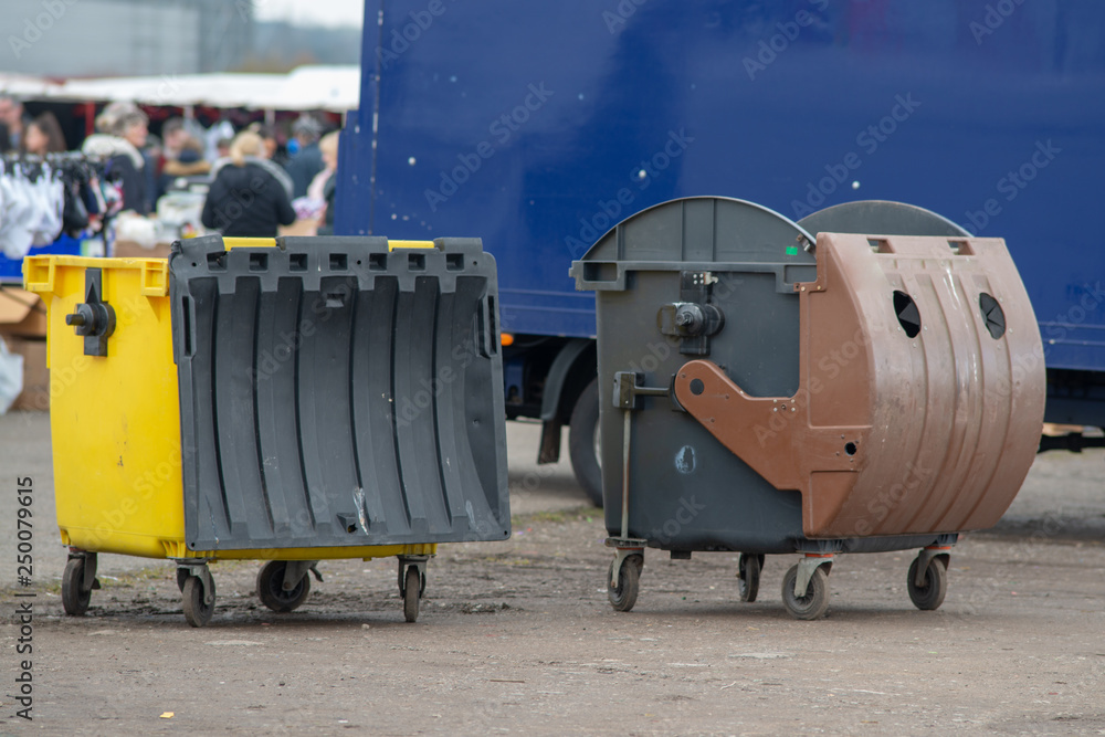 two large bins at market with people and and blue van in the backround
