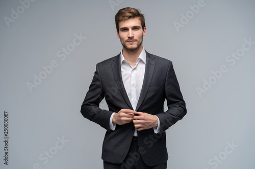 Canvastavla Portrait of serious handsome man in gray suit buttoning jacket against gray back