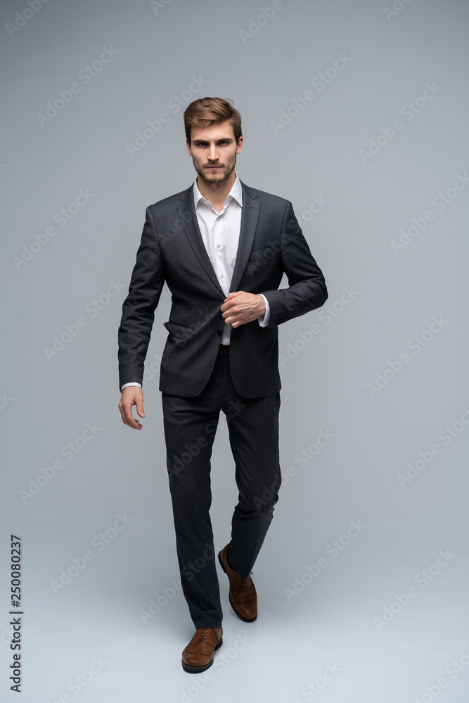 Perfect man. Full length of handsome young man in full suit buttoning his jacket and looking at camera while standing against gray background. Perfect man. Full length of handsome young man in full suit buttoning his jacket and looking at camera while standing against gray background.