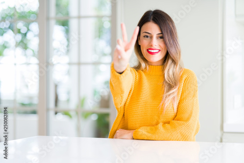 Young beautiful woman wearing winter sweater at home showing and pointing up with fingers number two while smiling confident and happy.