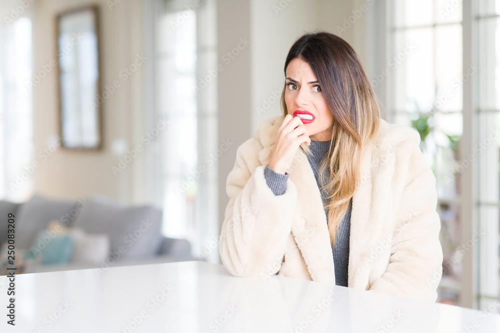 Young beautiful woman wearing winter fur coat at home looking stressed and nervous with hands on mouth biting nails. Anxiety problem. Young beautiful woman wearing winter fur coat at home looking stressed and nervous with hands on mouth biting nails. Anxiety problem.