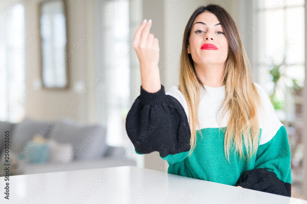 Young beautiful woman wearing winter sweater at home Doing Italian gesture with hand and fingers confident expression