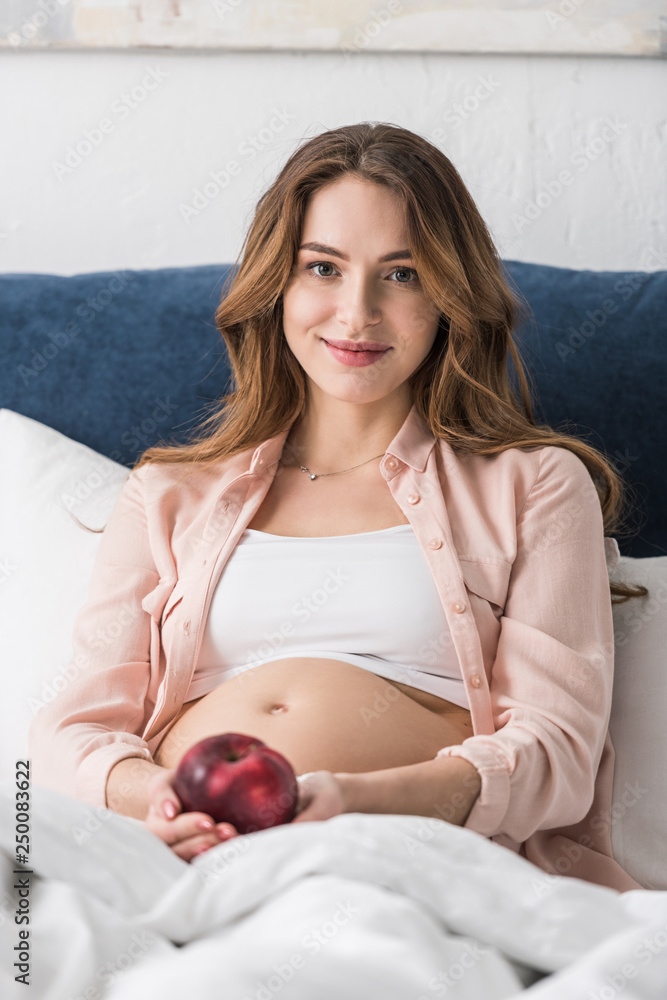 Happy pregnant woman lying in bed with apple and looking at camera Stock  Photo | Adobe Stock