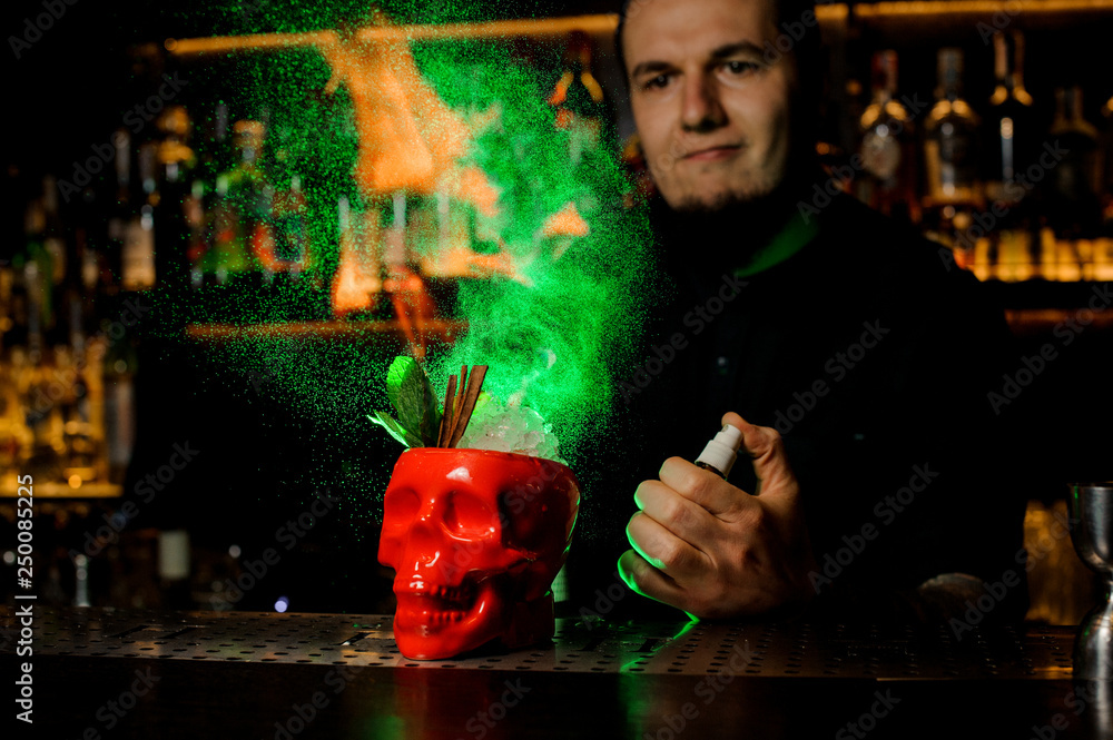 Bartender spraying on the cocktail in the red scull cup from the vaporizer and flame it