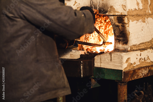 bearded man blacksmith gets a red-hot billet out of the furnace.