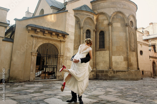 elegant wedding couple gently hugging and dancing in sunlight in old courtyard in european street. luxury bride and groom embracing. romantic sensual moment.