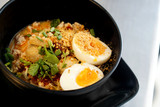 Thai spicy noodle or Tom Yum with boiled egg, vegetable, meat ball, mince pork, chilli and peanut, served in black bowl