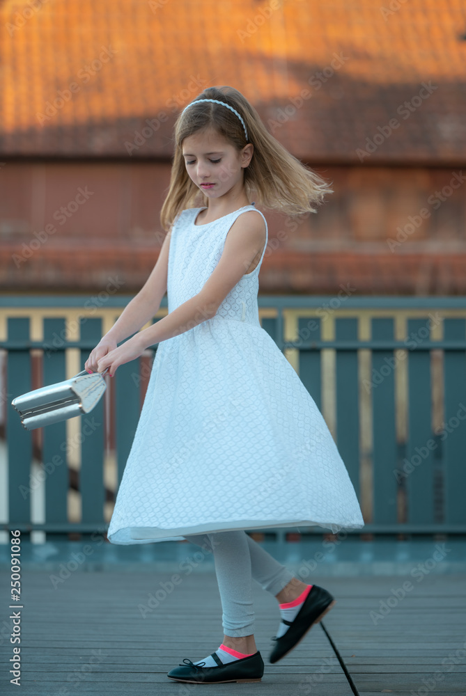 a little girl with blond hair in a white dress dances on the terrace on a sunny evening