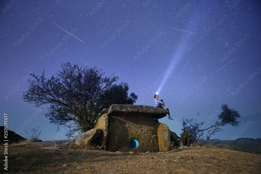 Young woman sitting on top of ancient Dolmen and looking at starry sky.