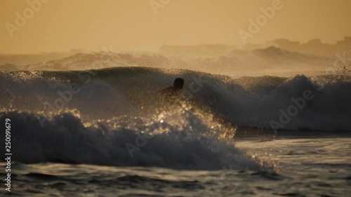 Surfer surfing during a sunset at a surfspot in Bali. Full HD footage in slow-motion. photo