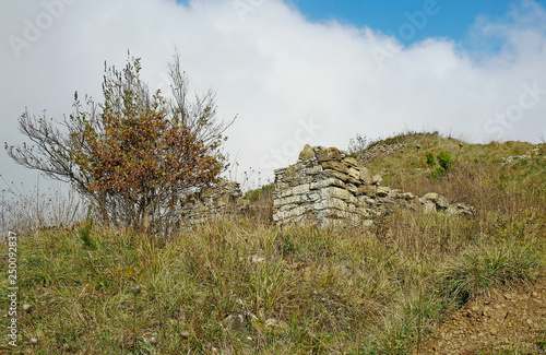 Il rudere di una casa in pietra su una collina aspra e verde.