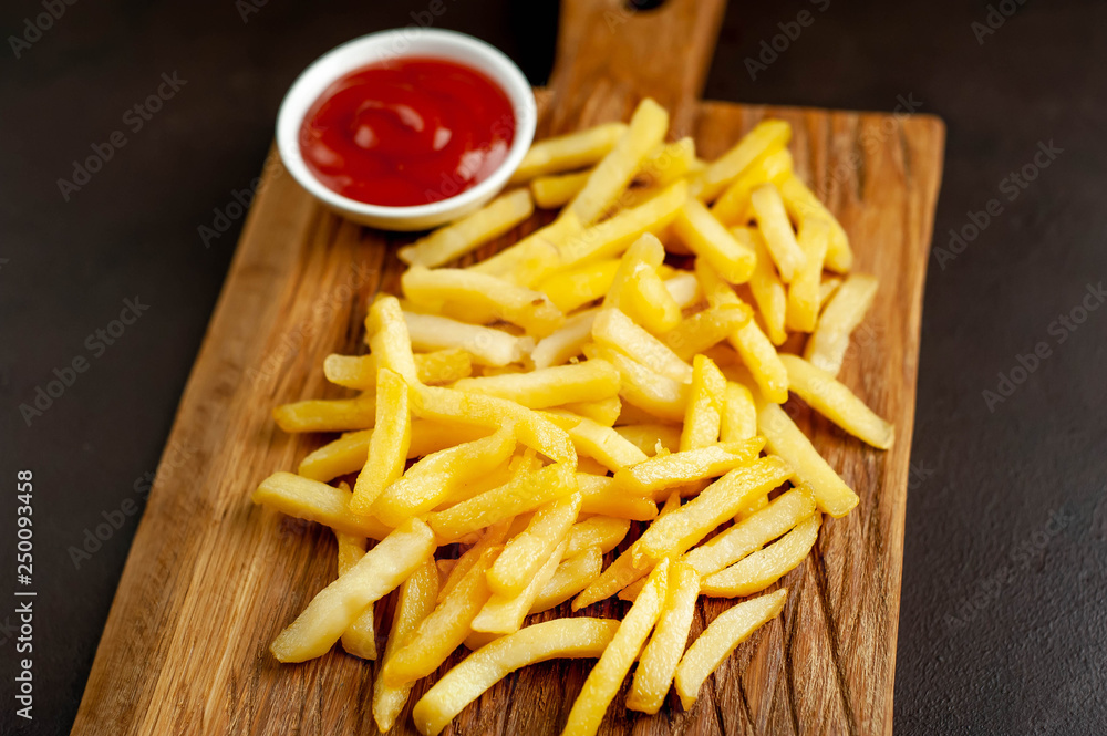 French fries with ketchup on a cutting board, background is concrete French fries with ketchup on a cutting board, background is concrete