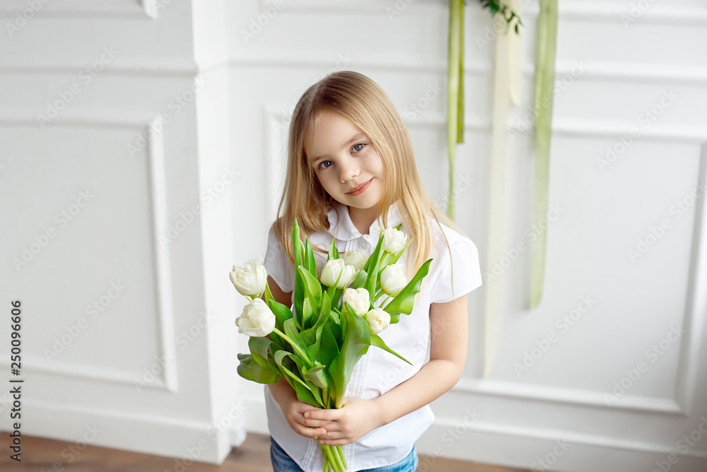 Portrait of a very cute pretty blonde girl in a white shirt against a white wall with a bouquet of white tulips Portrait of a very cute pretty blonde girl in a white shirt against a white wall with a bouquet of white tulips
