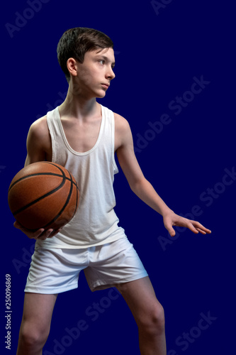 Teenager in a white T-shirt with a basketball ball on a blue background. Athlete guy. Sports team game, healthy lifestyle.