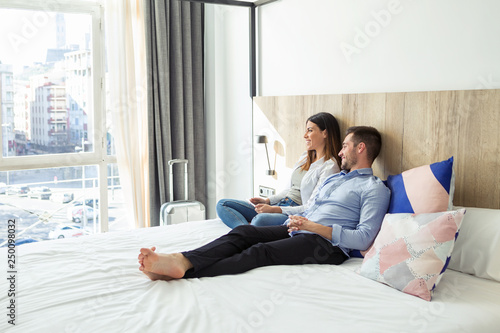 Beautiful lovely young couple lying and relaxing on bed looking sideways at hotel room. photo