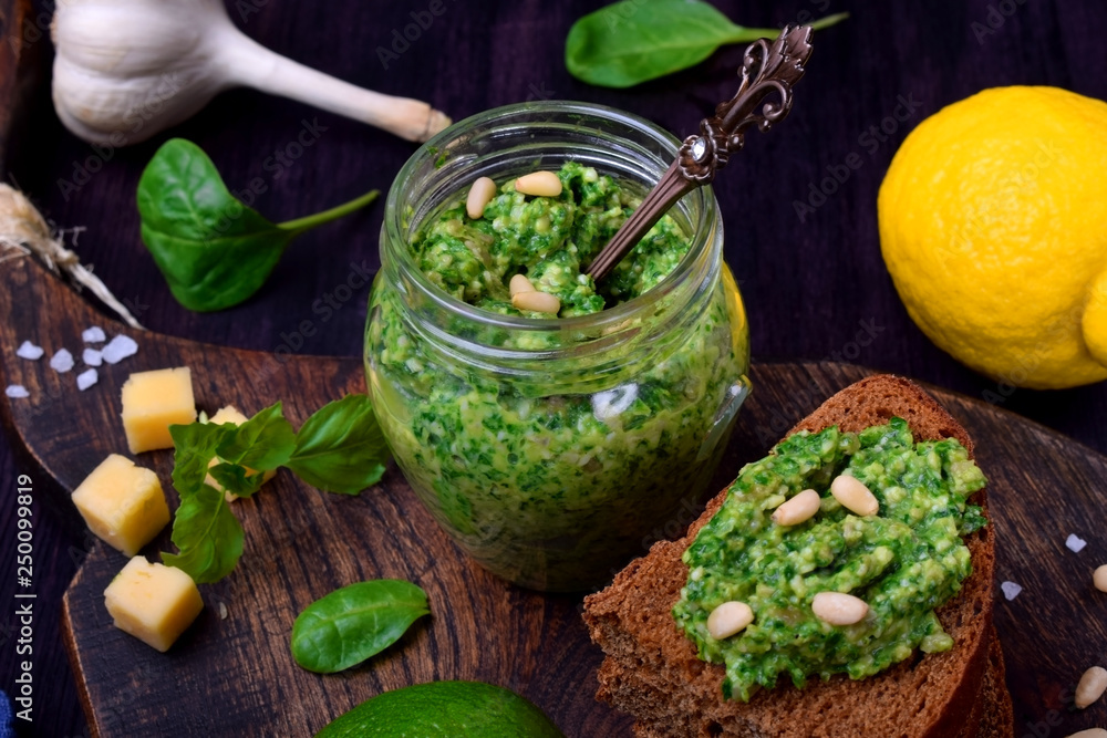 Green pesto in a jar and on a piece of bread surrounded by the ingredients