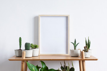 Stylish room interior with mock up photo frame on the brown bamboo shelf with beautiful plants in differents hipster and design pots. White walls. Modern and floral concept of shelfs.