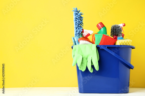 Bottles with detergent and cleaning tools on yellow background