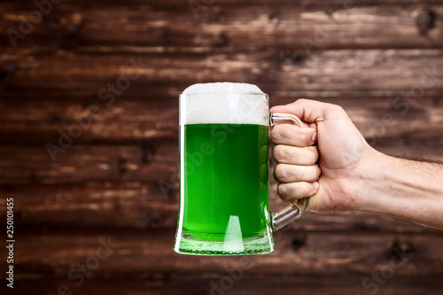 St. Patrick's Day. Glass mug with green beer in male hand on wooden background