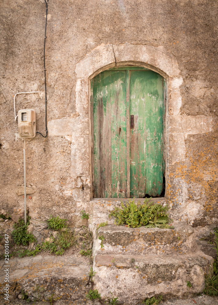 Fototapeta premium Wooden doors in green color with weathered paint and stone steps before it on the island Kyhtira, Greece