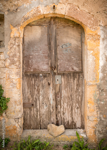 Stone in heart shape lying before old weathered doors in old brick wall on the island Kythira, Greece, alle in yellow and brown color