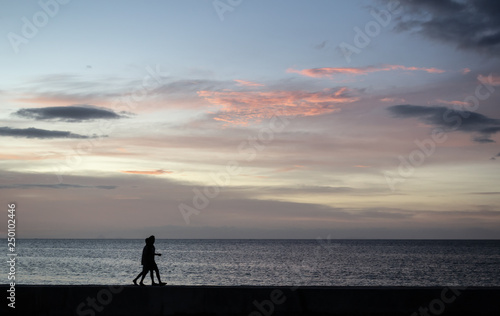 Silhouettes of the Couple of kids walking at the seafront during sunset