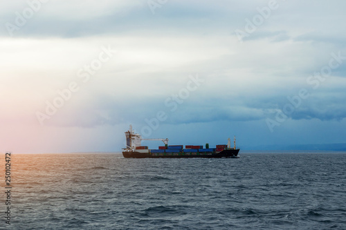 Cargo ship barge with containers on the sea horizon at sunset