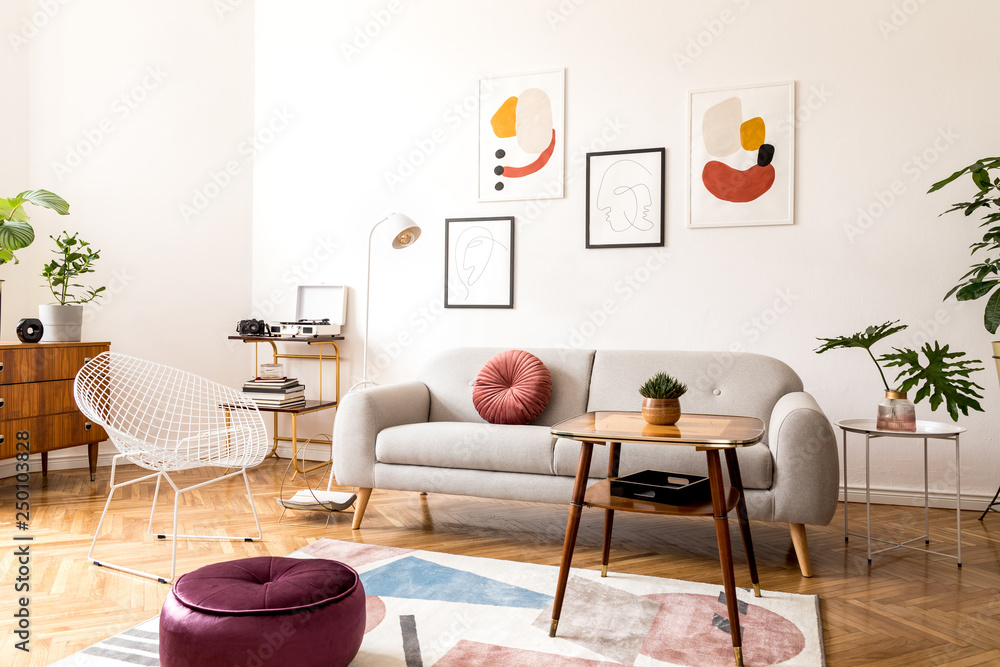 Minimal retro interior design of living room with grey couch, design armchair vintage coffee table, lamp and stylish decorations. Bright room, brwon wooden parquet and poster gallery on the wall.