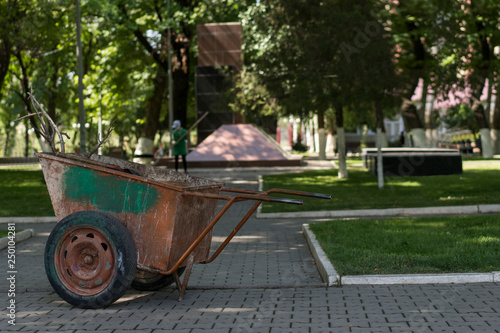 A shabby metal wheelbarrow for garbage disposal in the park.