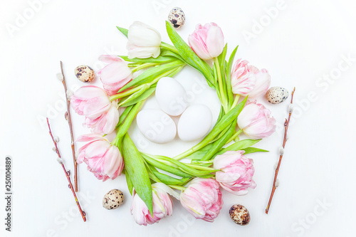 Spring greeting card. Easter eggs in nest and pink fresh tulip flowers bouquet on rustic white wooden background. Easter concept. Flat lay top view copy space. Spring flowers tulips