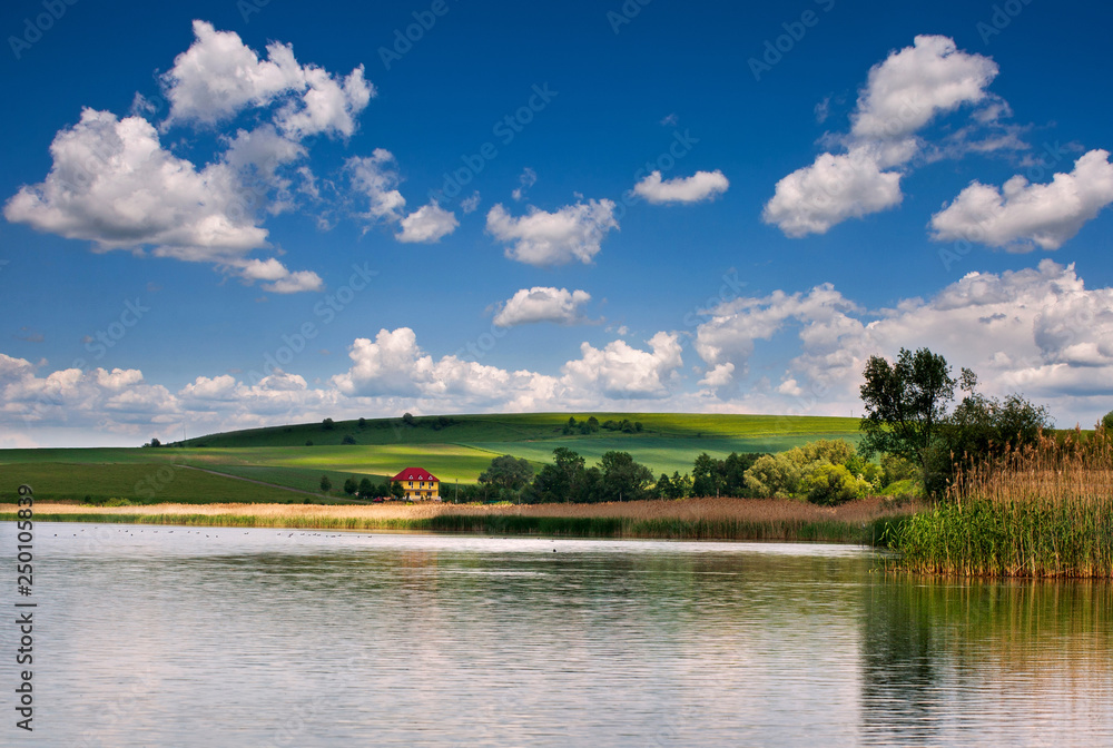 Rural countryside landscape lake green fields and pastures on background of blue sky clouds Rural countryside landscape lake green fields and pastures on background of blue sky clouds