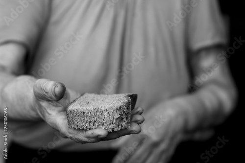an old grandmother stretches out a crust of bread in black and white art photography with a wrinkled hand
