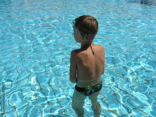 European boy prepares to swim in swimming pool. Healthy boy stands in swimming pool , European young kid training with swim goggles 