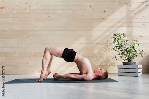 Sporty man practicing yoga on yoga class, bridgepose photo