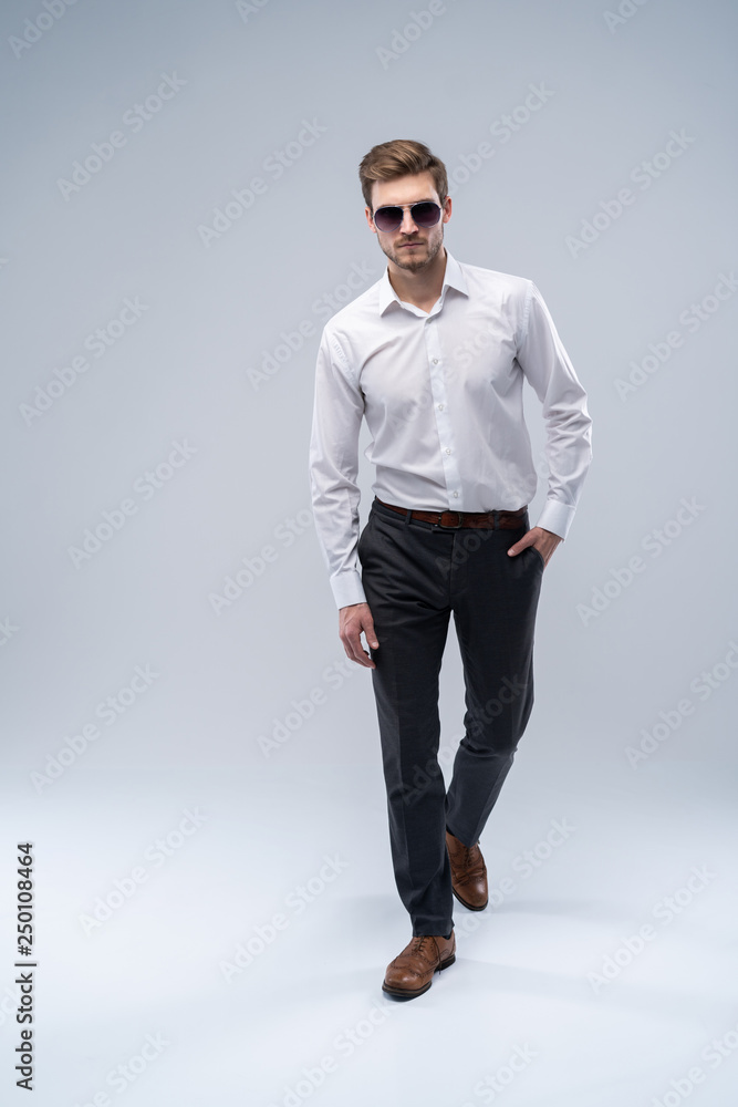 young man in sunglasses looks to side while walking on gray studio background. young man in sunglasses looks to side while walking on gray studio background.