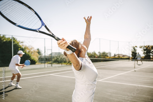 Senior woman making a serve while playing tennis © Jacob Lund