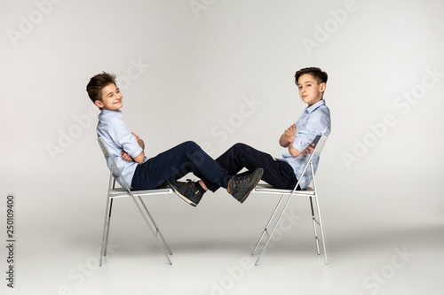 Two boys teenagers in blue shirts sitting on chairs