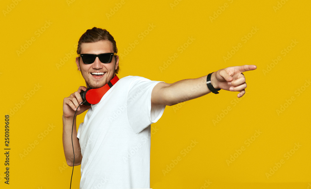 Cheerful man with headphones standing on yellow background and pointing away with index finger. Cheerful man with headphones standing on yellow background and pointing away with index finger.