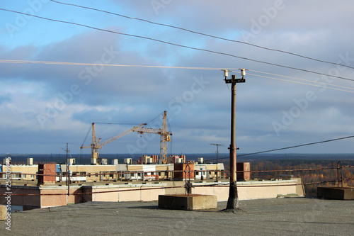 view from the flat roof of a multistory building covered with ruberoid, railing. column with electrical wires. view of the city of Arkhangelsk, construction cranes.