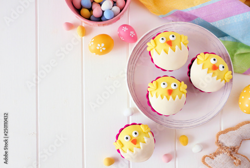 Hatching spring chick cupcakes. Flay lay table scene with copy space against a white wood background.