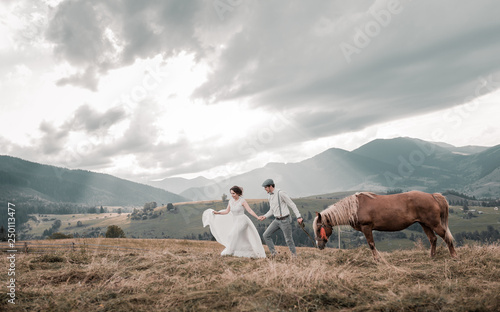 Rural wedding in the mountains. newlyweds dressed in wedding clothes with a horse on the background of mountains. Mountain range at sunset. Beautiful couple with mountains amazing view